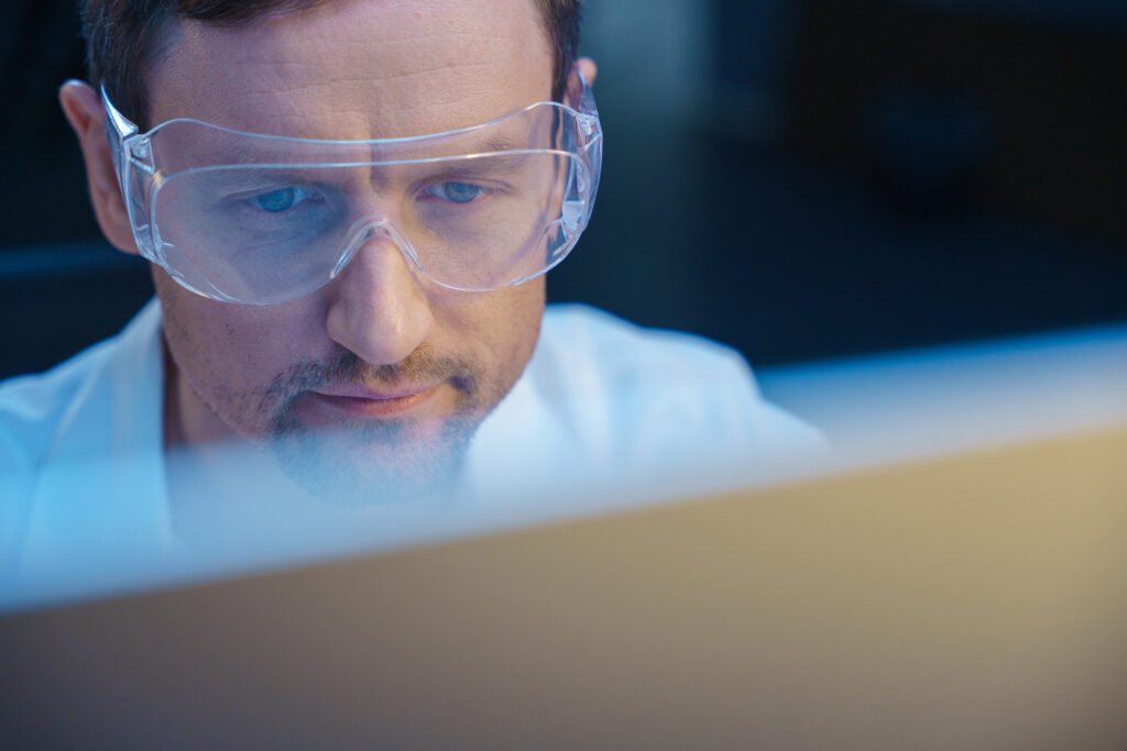 A young concentrated scientist looks into monitor, sitting in a modern lab, we see him in close-up